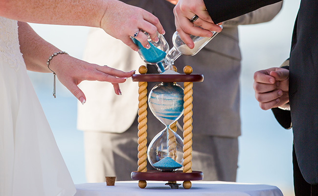 Bride and Groom pouring two different colors of sand into an hourglass vase at their Beach Wedding